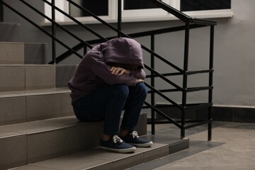 Child abuse. Upset boy sitting on stairs indoors