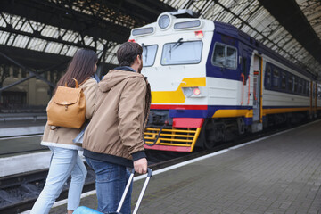 Being late. Couple with suitcase running towards train at station, back view. Space for text