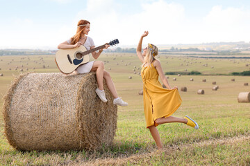 Beautiful hippie woman dancing while her friend playing guitar in field, space for text