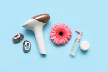 Poster Modern photoepilator with gerbera flower, attachments and cosmetic products on blue background © Pixel-Shot