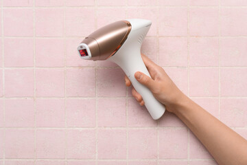 Female hand with modern photoepilator on pink tile background