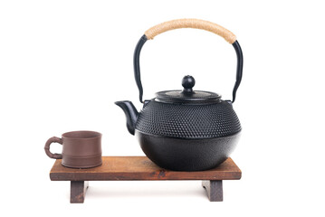 Traditional cast iron Asian teapot with clay cup on wooden stand on white background
