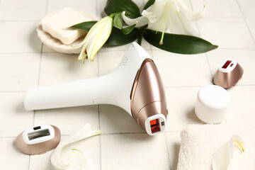 Fototapeta premium Modern photoepilator with attachments, bath supplies and lily flowers on white tile background
