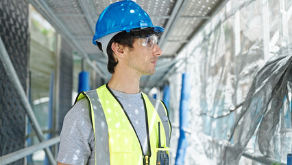 Young hispanic man architect wearing hardhat standing with serious face at construction place