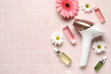 Obraz na płótnie Canvas Modern photoepilator with bottles of cosmetic oil and beautiful flower on pink tile background