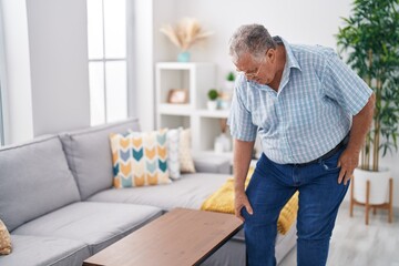 Middle age grey-haired man suffering for knee injury standing at home