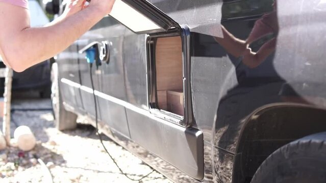 Caucasian man in red t-shirt pulling out the cassette toilet of a black camper van to empty disposal waste. High quality FullHD footage. Lifestyle sewage shot