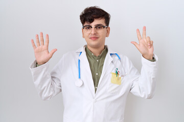 Young non binary man wearing doctor uniform and stethoscope showing and pointing up with fingers number eight while smiling confident and happy.