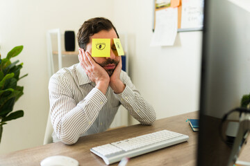Tired hispanic boss sleeping at work using funny sticky notes