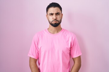 Hispanic young man standing over pink background puffing cheeks with funny face. mouth inflated...