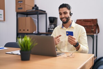 Hispanic young man wearing call center agent headset doing online shopping smiling happy pointing...