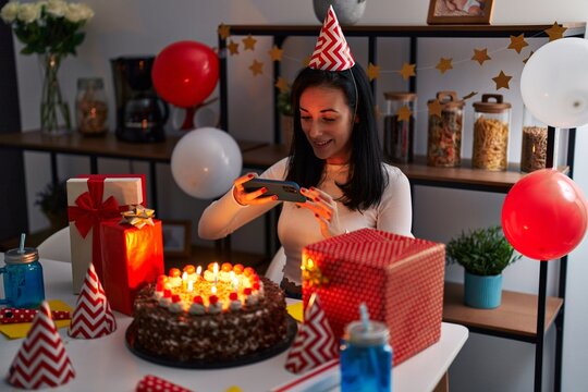 Young caucasian woman celebrating birthday make photo to cake by smartphone at home