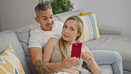 Man and woman couple using smartphone sitting on sofa at home