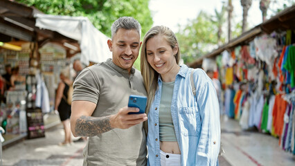 Naklejka premium Man and woman couple smiling confident using smartphone at street market