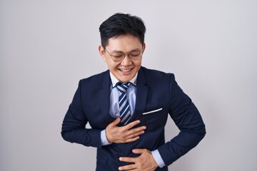 Young asian man wearing business suit and tie smiling and laughing hard out loud because funny...