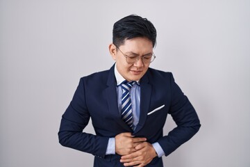 Young asian man wearing business suit and tie with hand on stomach because indigestion, painful illness feeling unwell. ache concept.