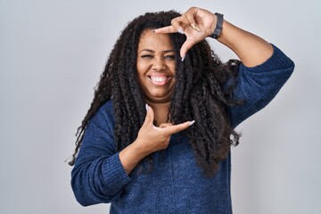 Plus size hispanic woman standing over white background smiling making frame with hands and fingers...