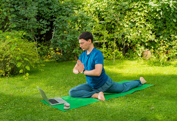 yoga man on a natural green background performs exercises using a laptop
