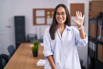 Young hispanic woman at the office showing and pointing up with fingers number five while smiling...