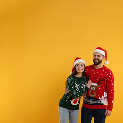 Fototapeta premium Happy young couple in Christmas sweaters and Santa hats on orange background. Space for text