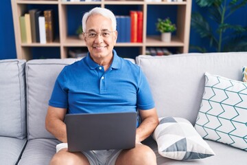 Middle age grey-haired man using laptop sitting on sofa at home