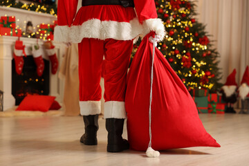 Fototapeta na wymiar Santa Claus holding bag of presents in room with Christmas tree, closeup