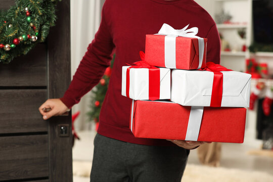 Young man in Santa hat with Christmas gift boxes indoors, closeup. Sending present by mail