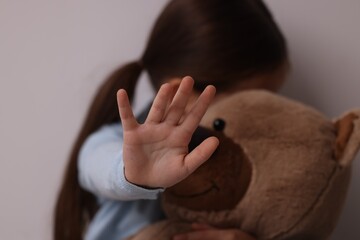 Child abuse. Little girl with teddy bear doing stop gesture on light grey background, selective focus