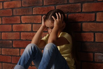Child abuse. Upset little girl near brick wall