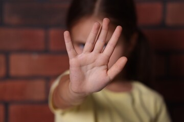 Child abuse. Little girl doing stop gesture near brick wall, selective focus