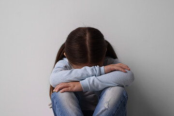 Child abuse. Upset little girl near light grey wall
