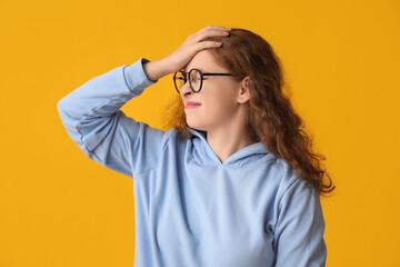 Portrait of worried young woman covering face with hand on yellow background