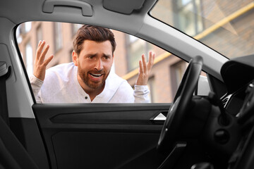 Automobile lockout, key forgotten inside. Emotional man looking through car window