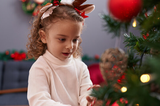 Adorable blonde girl wearing reindeer ears decorating christmas tree at home