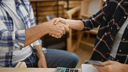 Two hearty carpenters, handing over dollars, seal a woodwork agreement with a firm handshake at...