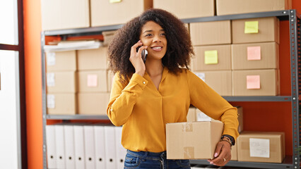 African american woman ecommerce business worker holding package talking on smartphone at office