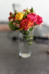 A bouquet of decorative roses stands on the table in a transparent glass. A soft focus on a bouquet of colorful roses.