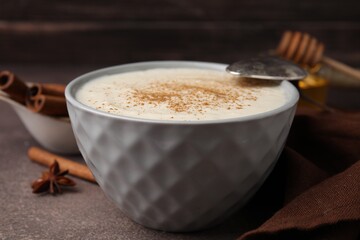Delicious semolina pudding with cinnamon in bowl and spoon on brown table, closeup