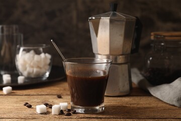 Brewed coffee in glass, moka pot, beans and sugar cubes on wooden table