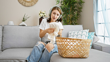 Young woman holding clothes of basket listening to music at home
