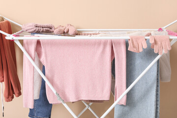 Dryer with winter clothes on beige background