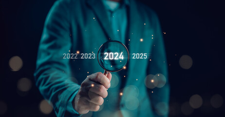 Businessman use magnifying glass search with 2024 wording for marketing monitor and business...