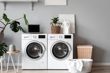 Interior of laundry room with washing machines, houseplants and laptop
