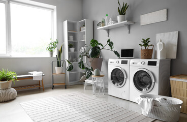 Interior of laundry room with washing machines, houseplants and laptop