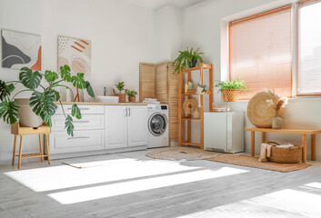 Interior of stylish laundry room with washing machine and houseplants