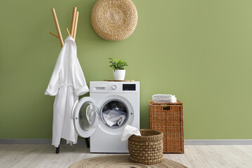 Laundry room interior with washing machine, wicker basket and bathrobe on rack - obrazy, fototapety, plakaty