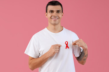 Handsome young man with red ribbon on pink background. World AIDS day concept