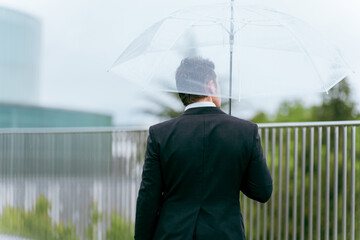雨の日に傘をさす外国人ビジネスマン（梅雨・台風・異常気象・天候）
