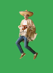 Handsome young man in poncho, sombrero and with guitar jumping on green background