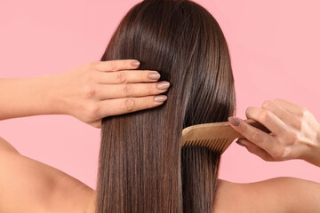 Young brunette woman combing beautiful hair on pink background, back view
